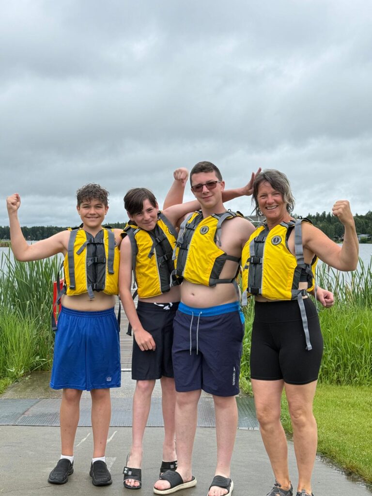 Three young men and a woman in life vests in front of a lake